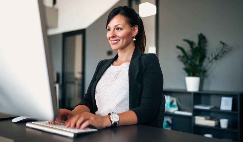 business administrator smiling sitting in front of a computer typing