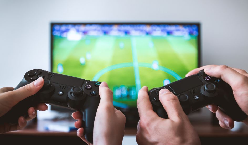 two hands holding video game controllers in front of a tv screen with a video game on display