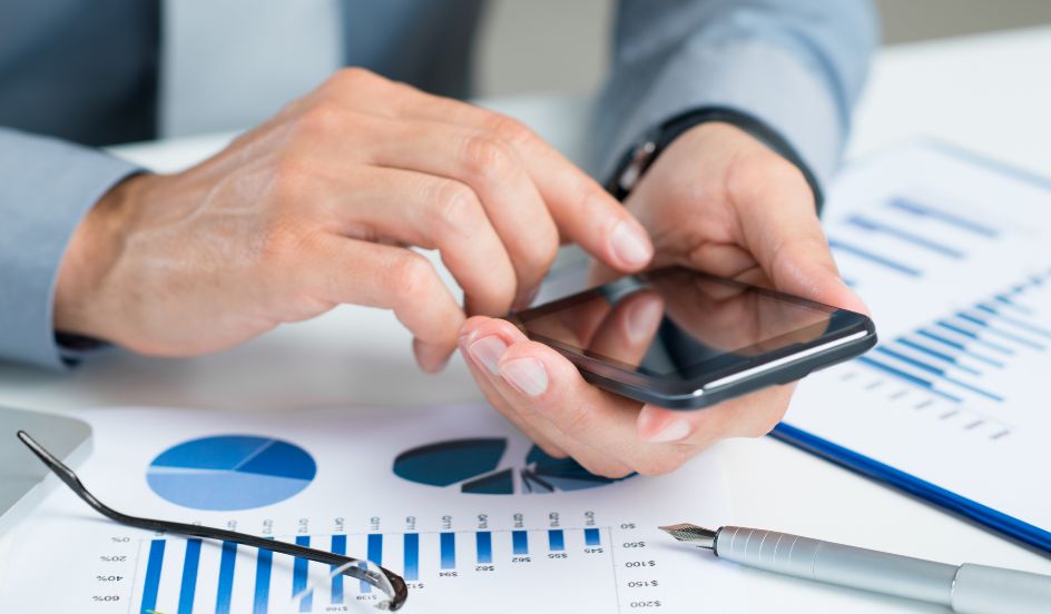 hands holding a cell phone above papers and graphs and data