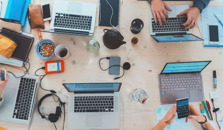 overhead view of table with people working on laptops and technology