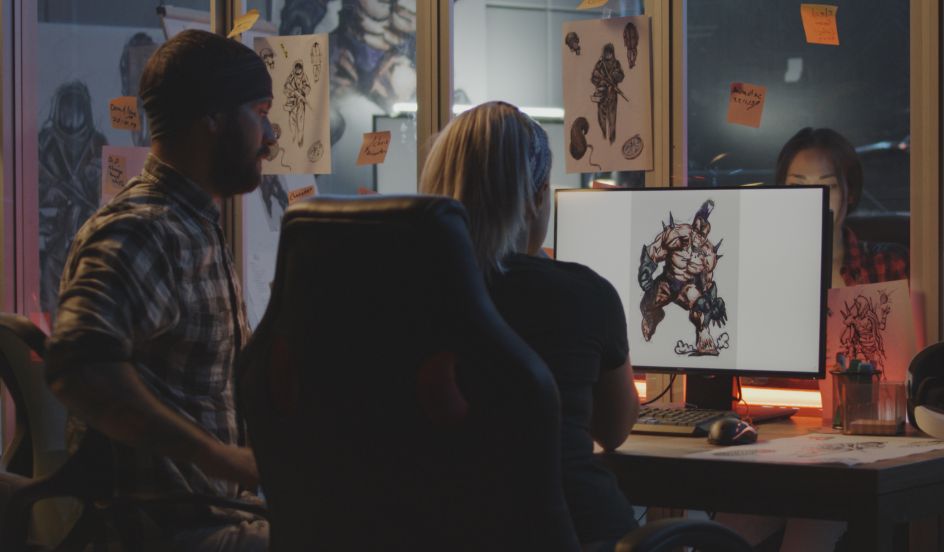 male and female sitting at computer with video game graphic displayed on screen