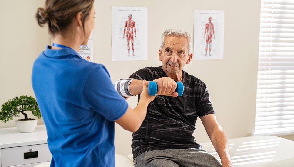 physiotherapist helping senior male hold a weight