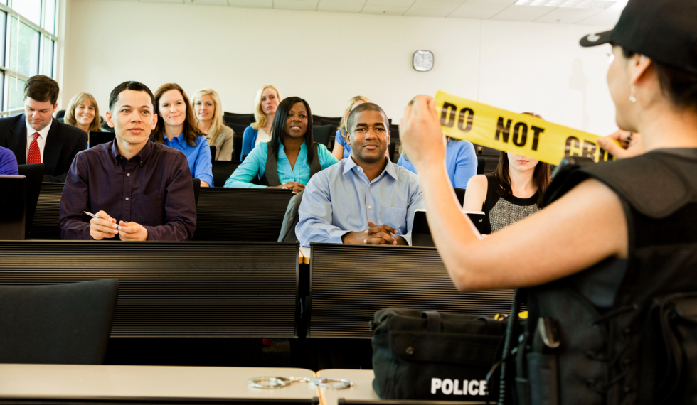 female police officer standing in front of classroom with students watching her hold up a piece of caution tape