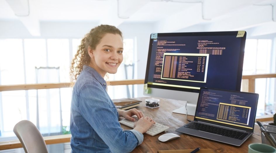 a woman in a blue shirt smiles as she types on a computer with code on it